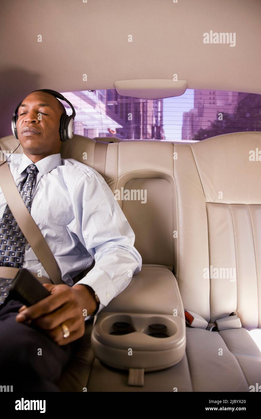 African businessman listening to headphones in back seat of car Stock Photo Alamy