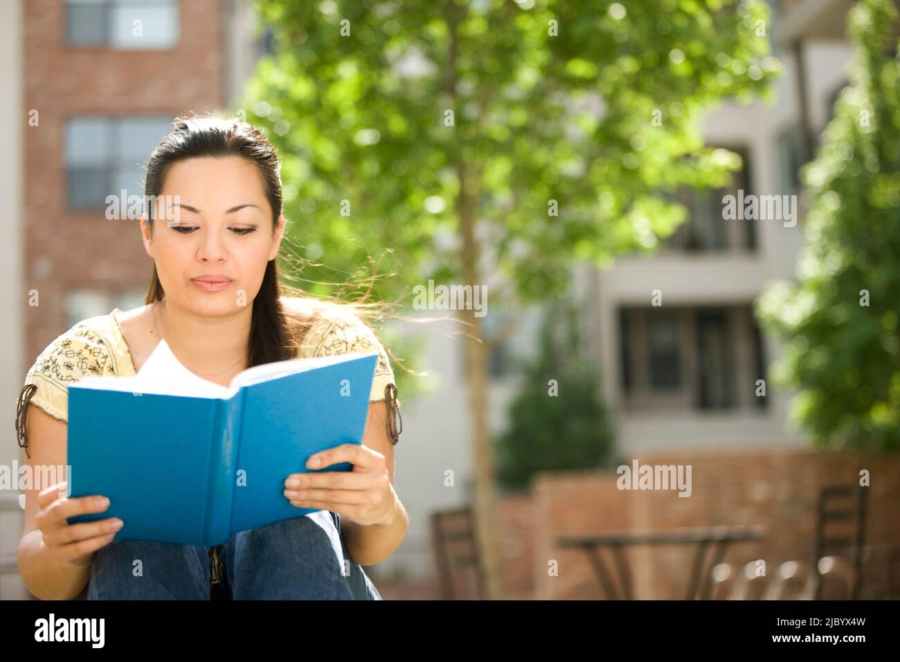 Mixed race woman reading book outdoors Stock Photo