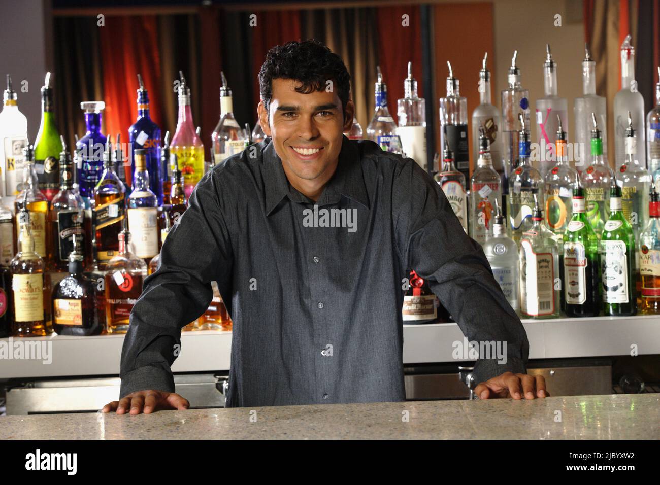 Hispanic male bartender leaning on bar Stock Photo