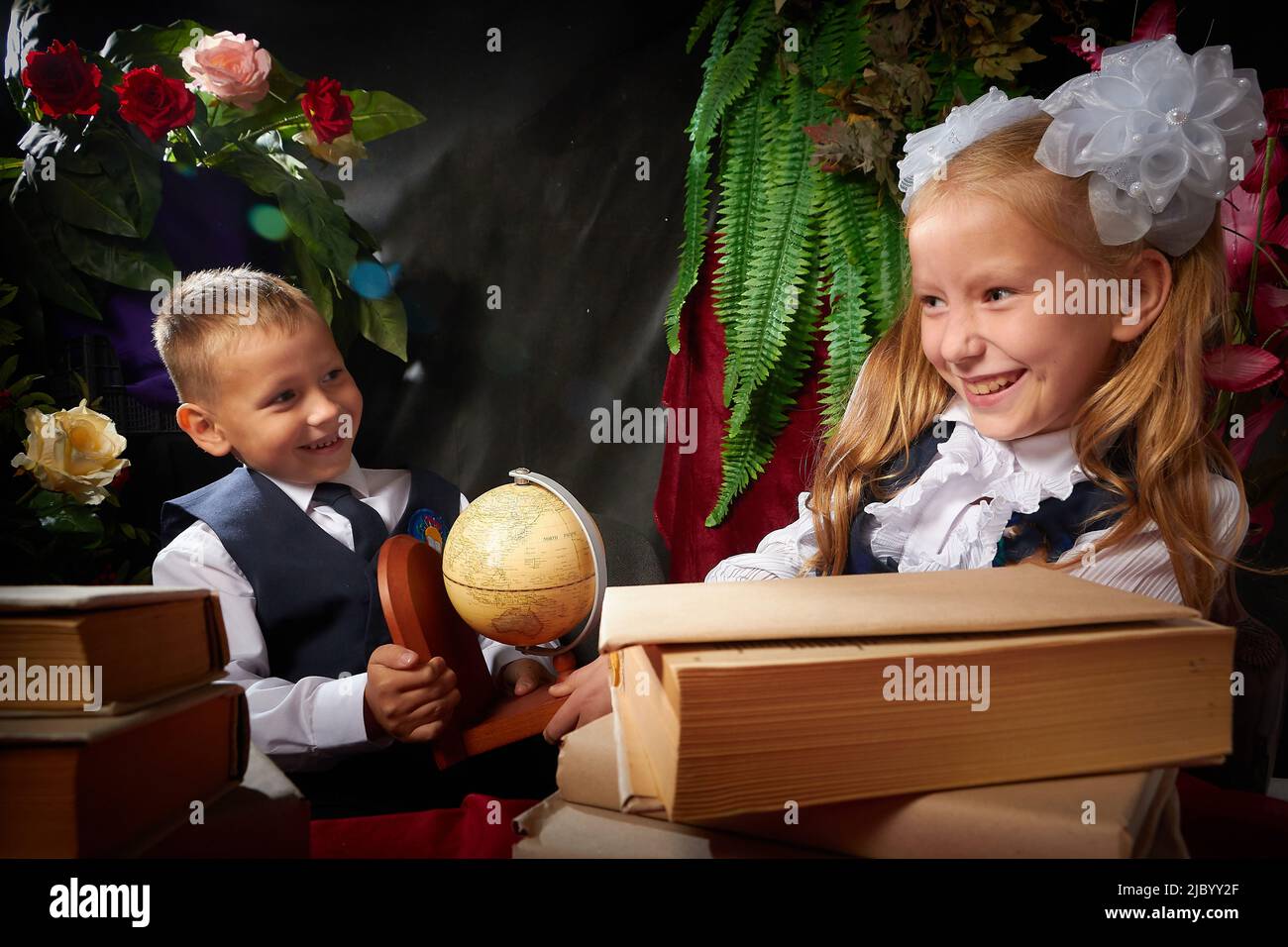Girl and boy who is elementary school children in uniform having fun on black background with flowers. Brother and sister on September 1 in Russia Stock Photo
