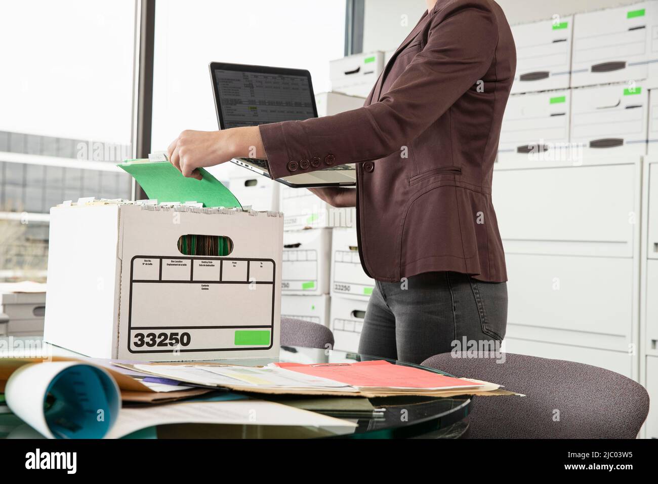 Tight shot of a woman holding a laptop sorting through a box. Stock Photo