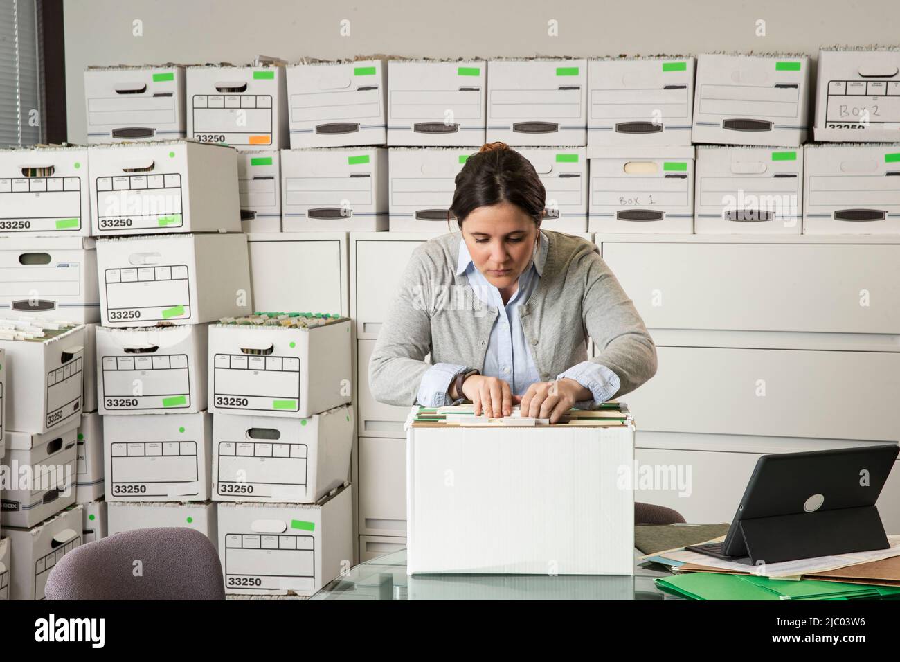 A woman looks through a box of files in an office Stock Photo