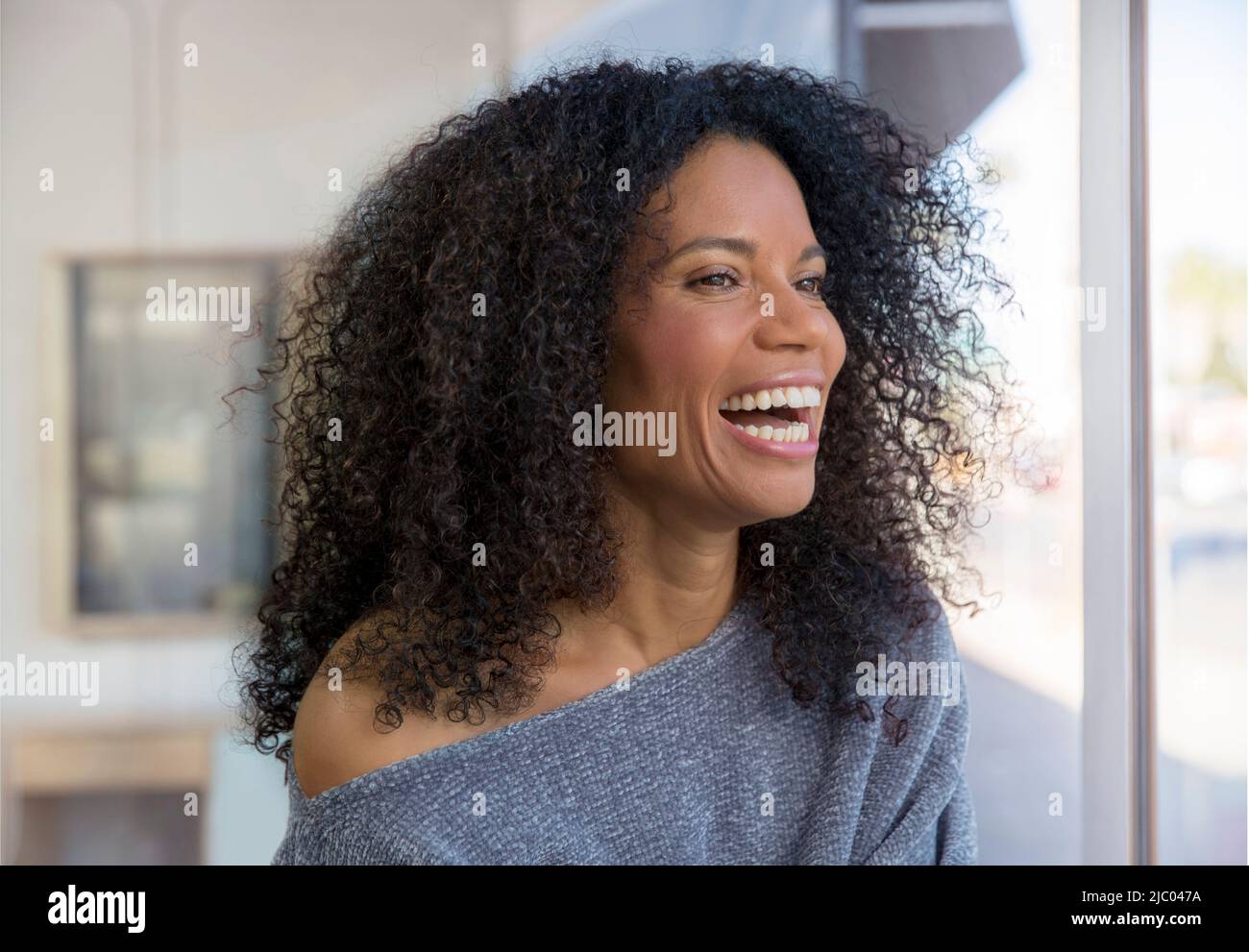 Mixed race, middle-aged woman laughing and looking out the window. Stock Photo