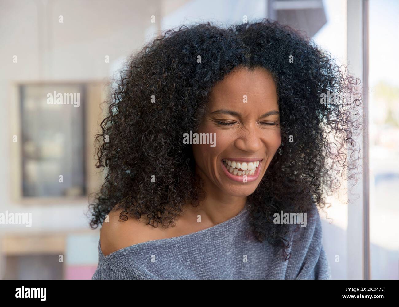 Mixed race, middle-aged woman laughing in a brightly lit room. Stock Photo