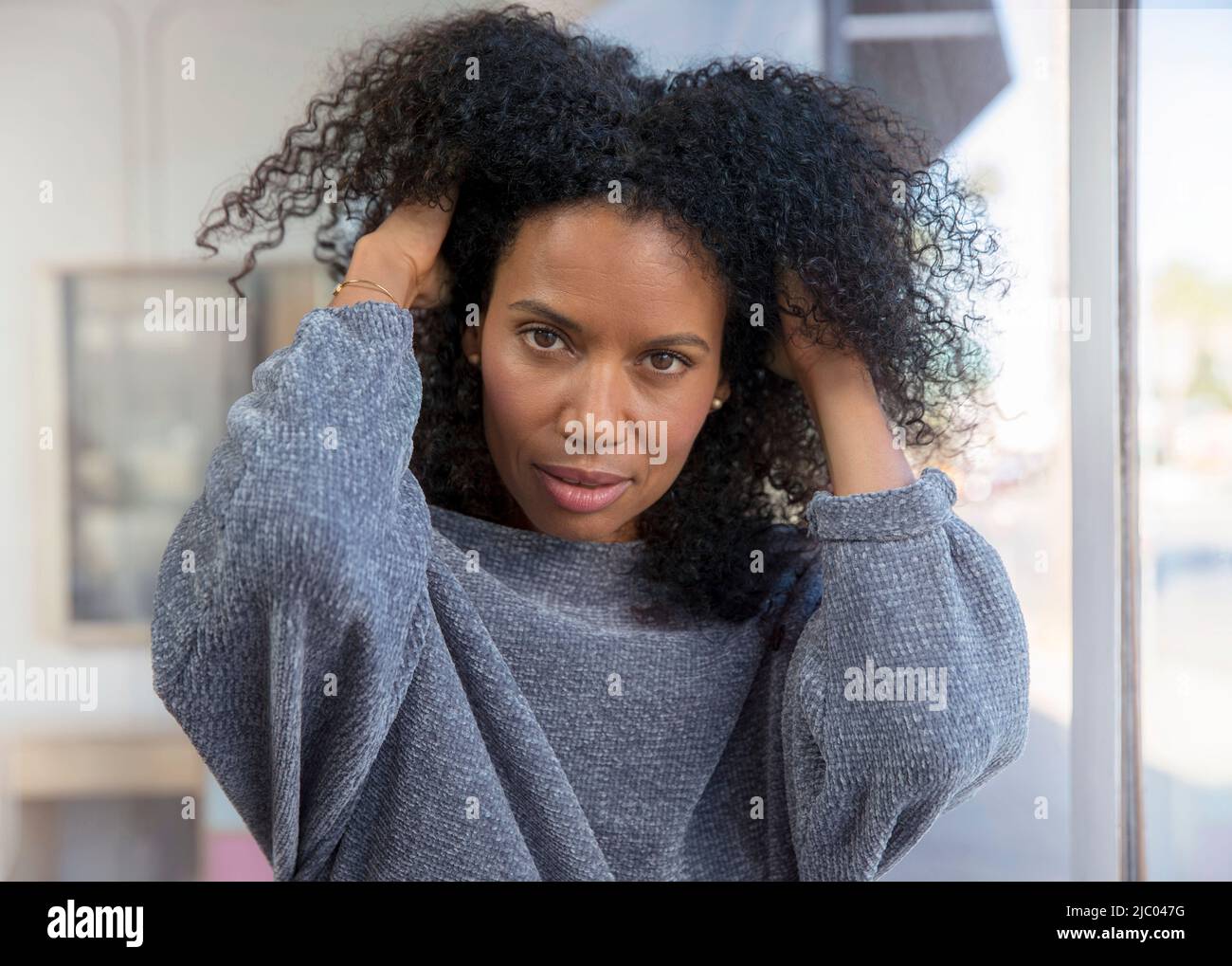 Mixed race, middle-aged woman runs her hands through her hair looking at the camera. Stock Photo