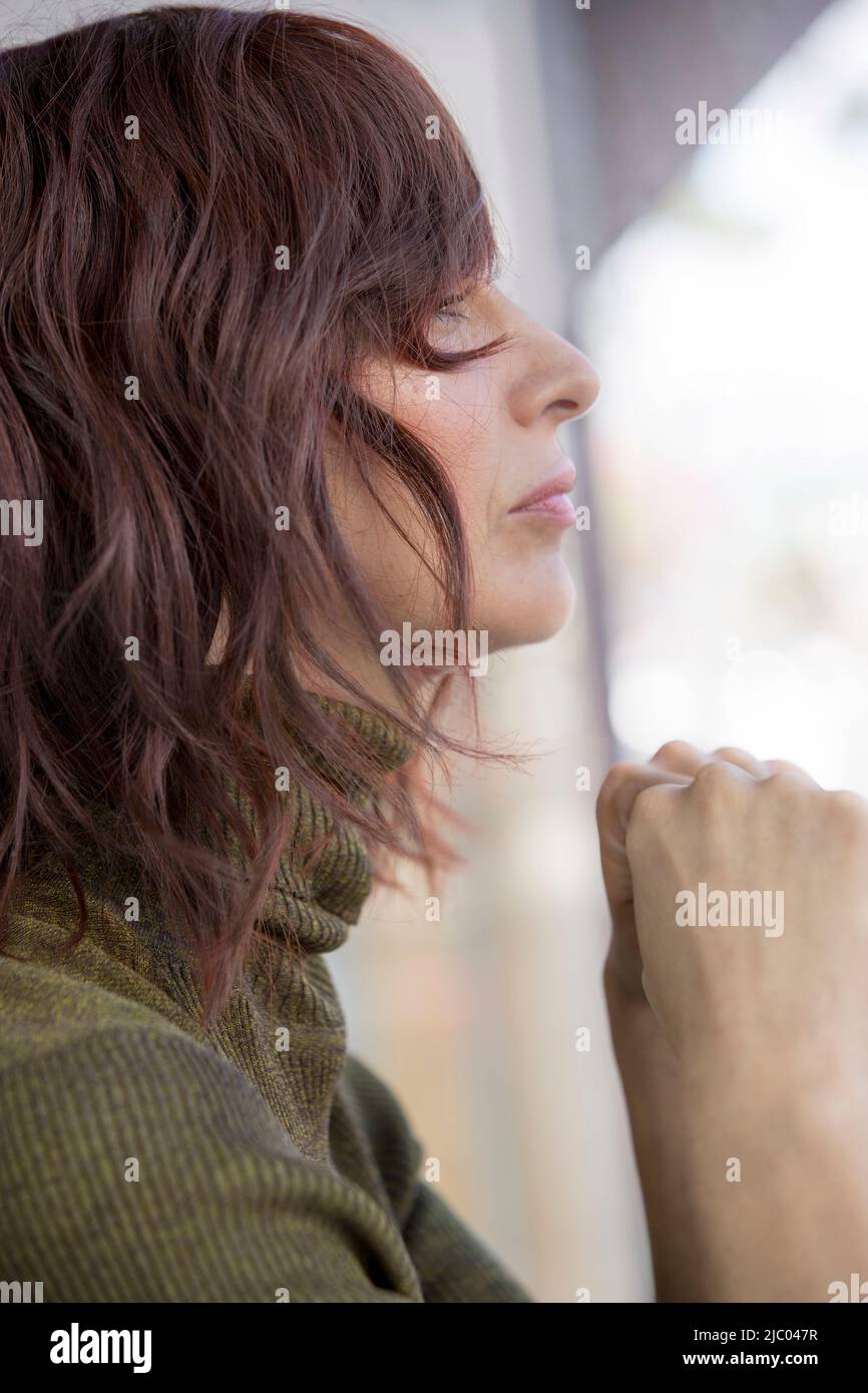 Close-up profile of a middle-aged woman with red hair looking out a window. Stock Photo