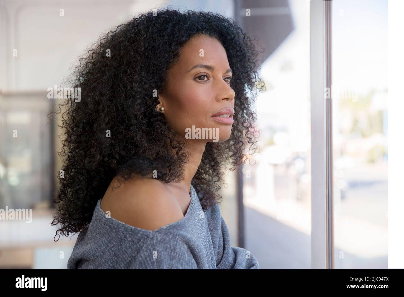 Middle-aged woman gazes thoughtfully out a window. Stock Photo