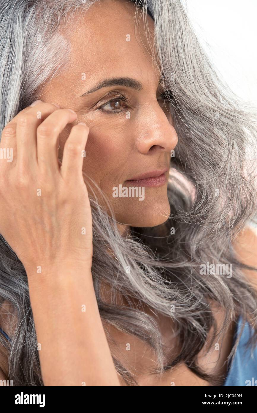 A middleaged woman with grey hair pulls her hair behind her ear Stock