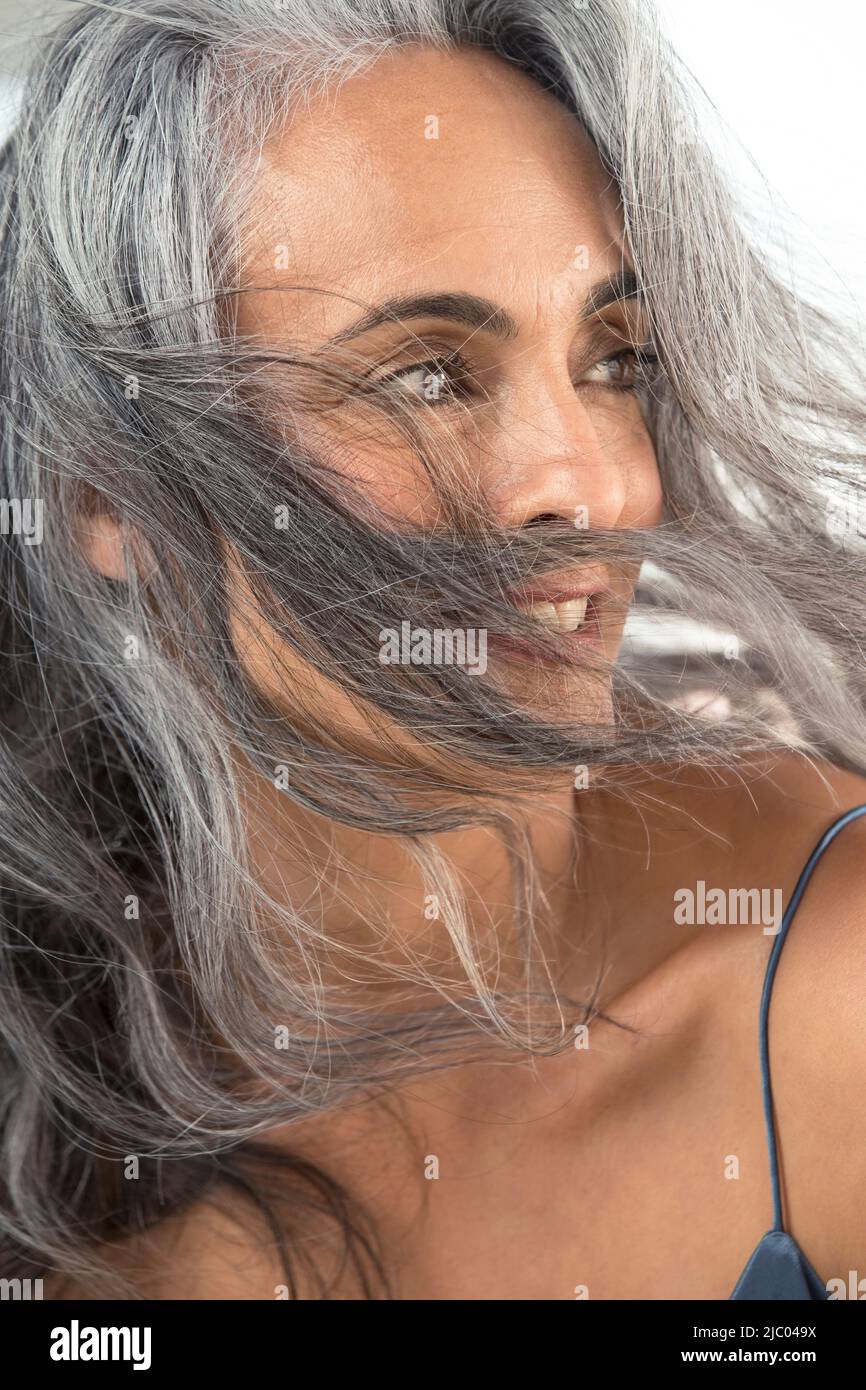 A youthful middle-aged woman looks to the right as wind blows her grey hair across her face. Stock Photo