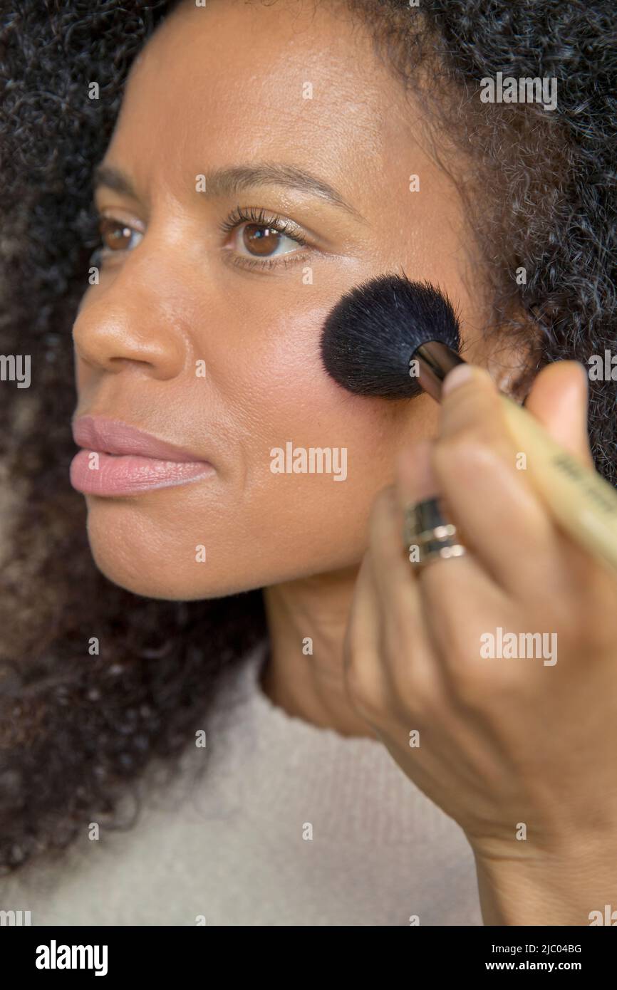 Mixed race, middleaged woman looks off camera while putting on make up