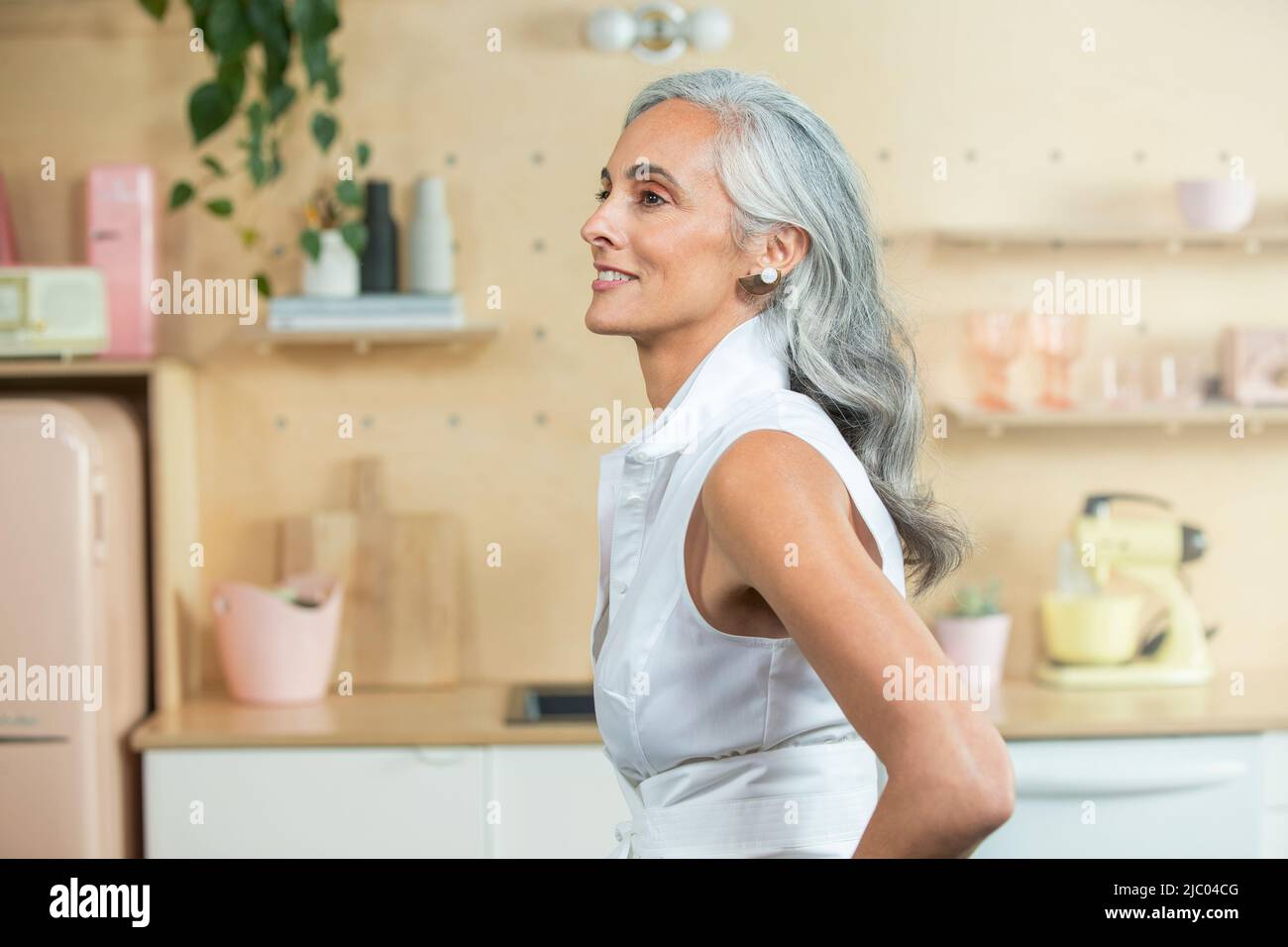Standing in a modern kitchen, A youthful middle-aged woman with gray hair looks off camera. Stock Photo
