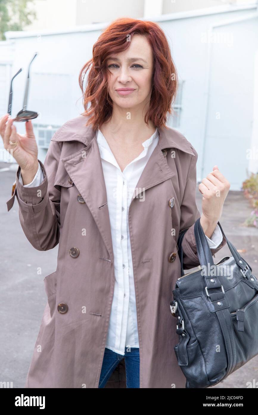 A middle-aged woman with red hair walking out of a building holding her sunglasses and purse. Stock Photo