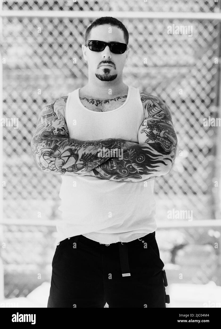 Portrait of a mid adult man standing wearing sun glasses with tattooed arms folded Stock Photo