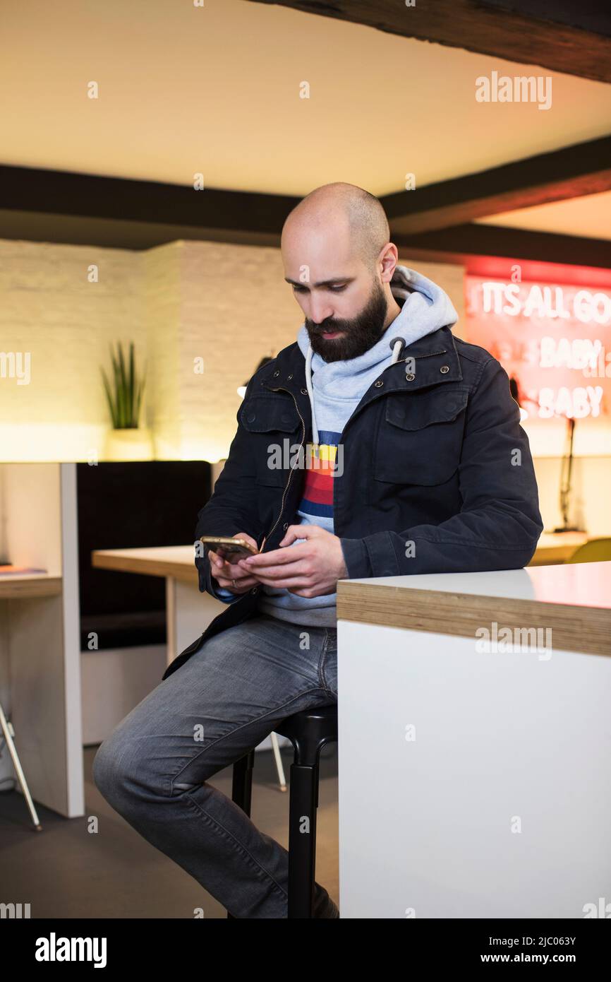 Man checking his phone while sitting at table in co-working space Stock Photo