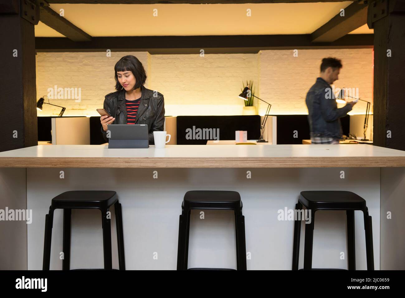woman sitting at counter checking her phone in co-working space Stock Photo