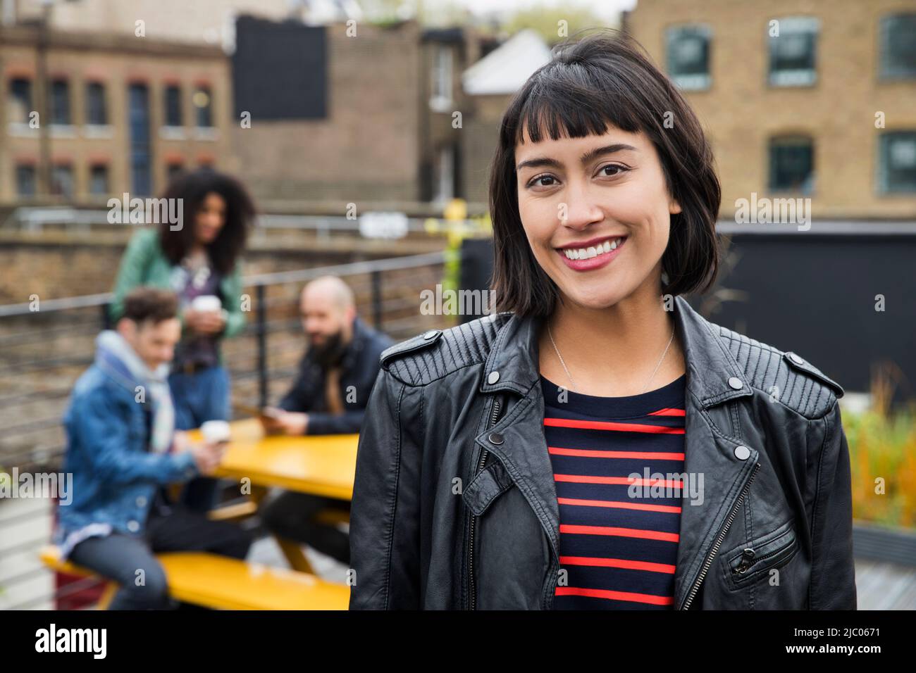 Portrait of Woman with group of friends working on tablets at outdoor patio table in co-working space in the background Stock Photo