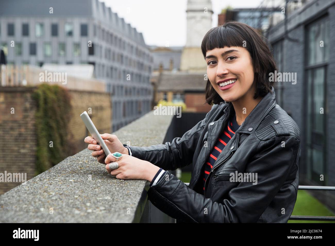 Woman on mobile phone standing at ledge of building on rooftop patio Stock Photo