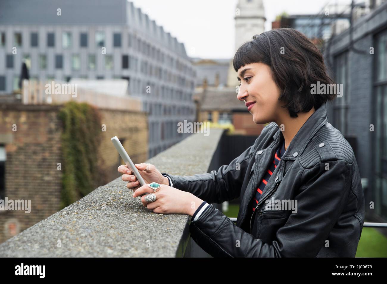 Woman on mobile phone standing at edge of building on rooftop patio Stock Photo