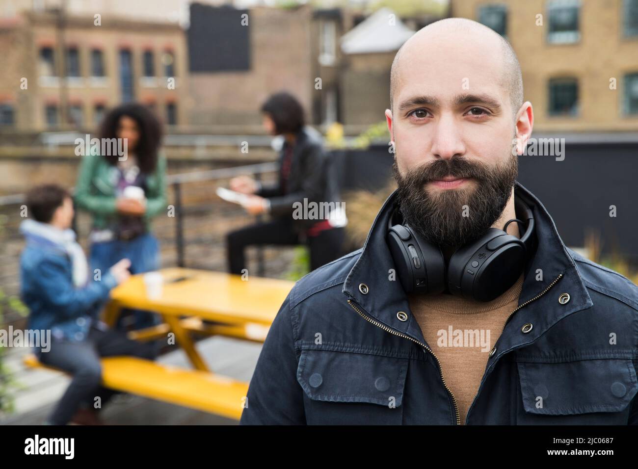 Portrait of man with group of friends working on tablets at outdoor patio table in co-working space in the background Stock Photo