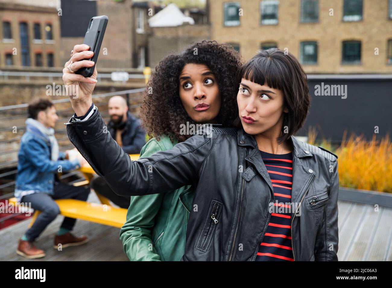 Portrait of Women on rooftop patio taking selfies with cell phone Stock Photo
