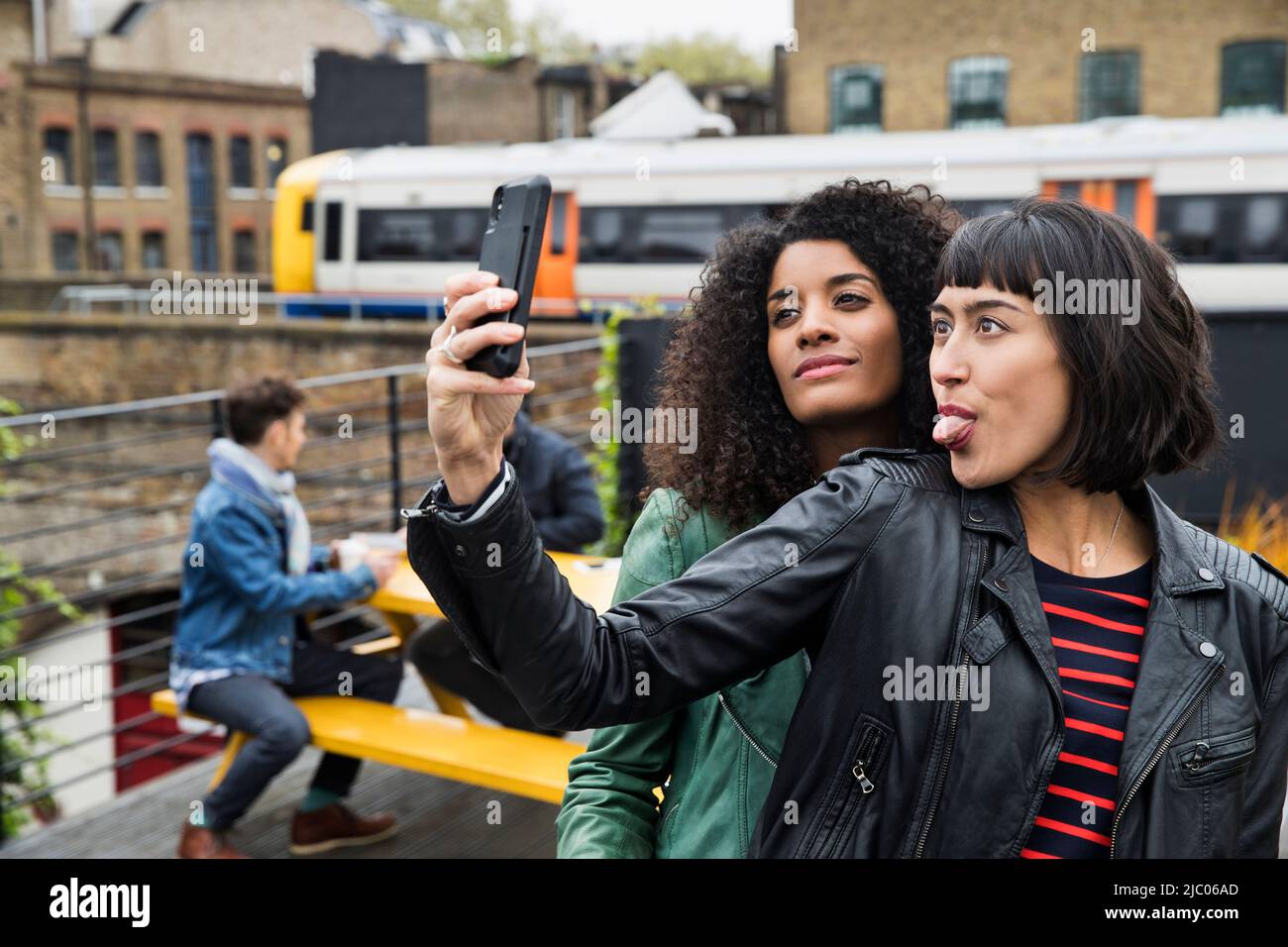 Portrait of Women on rooftop patio taking selfies with cell phone Stock Photo