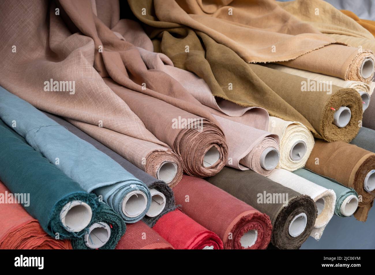 Fabric rolls of beige and brown material background. Old carton reels with colorful flax linen and canvas textile on a retail market stall, close up, Stock Photo