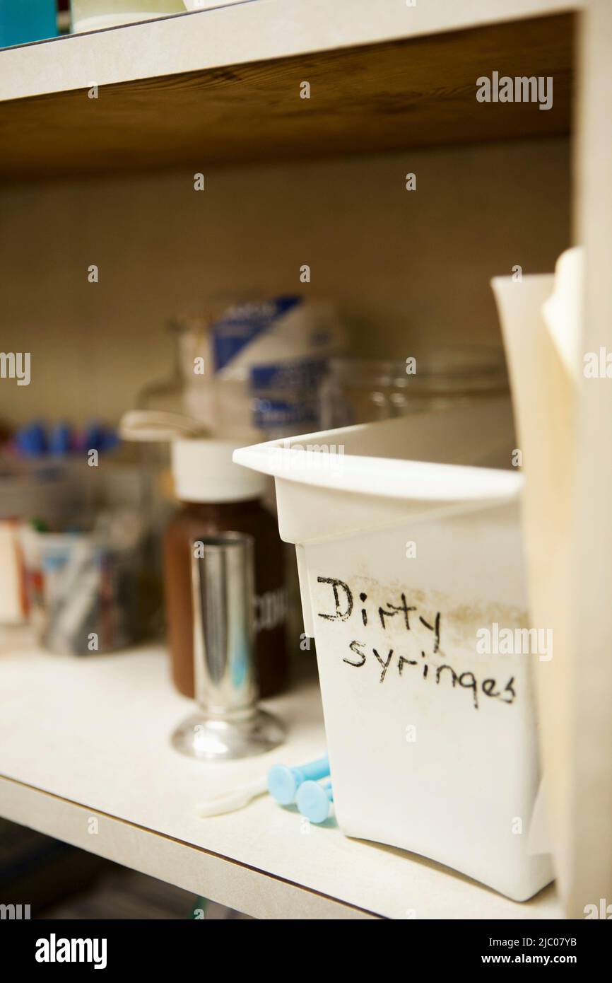 Plastic container labeled dirty syringes on a shelf at a clinic Stock