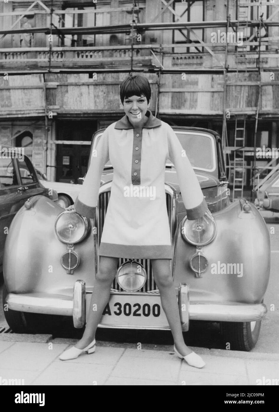 Mary Quant. Born 11 February 1930. British fashion designer and fashion icon. She became an instrumental figure in the 1960s London-based Mod and youth fashion movements.  She was one of the designers who took credit for the miniskirt and hotpants. Picture of her in front of the luxury car wearing a creation of her own with long wide sleaves and a length of the dress well above her knees. 1966 Stock Photo