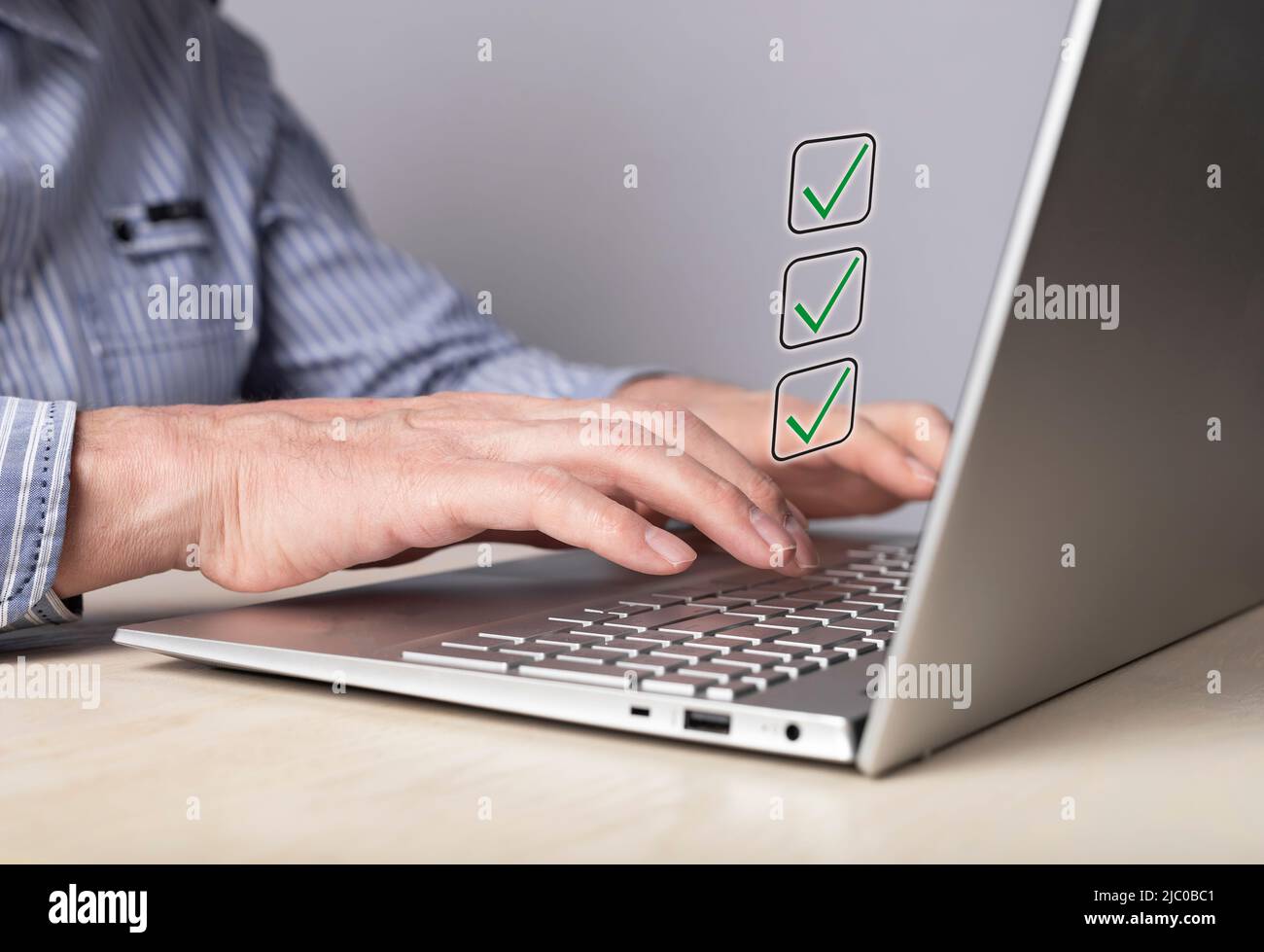 Man working on laptop and marking achieved goals with ticks or taking survey and noting right answers. Checklist, planning, time management concept. Male hands at computer keyboard. High quality photo Stock Photo