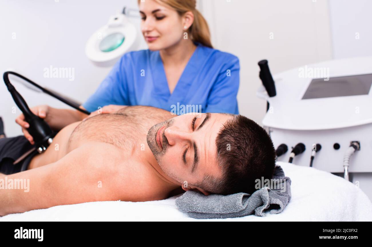 Qualified woman cosmetologist with male client during hardware body procedure in modern aesthetic clinic Stock Photo