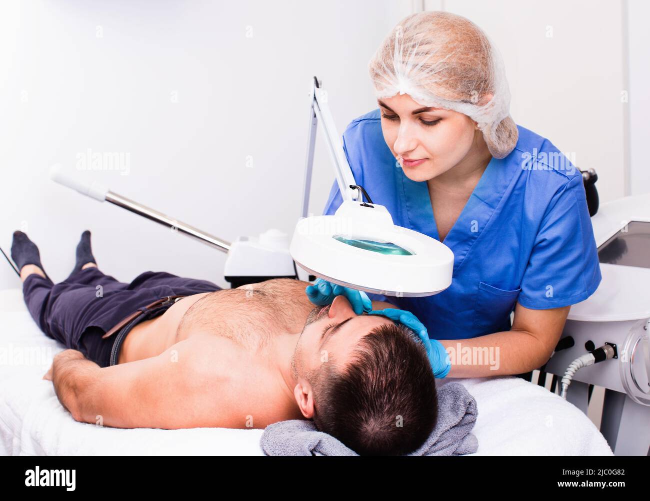 Confident woman cosmetologist examining male client face before procedure in esthetic clinic Stock Photo