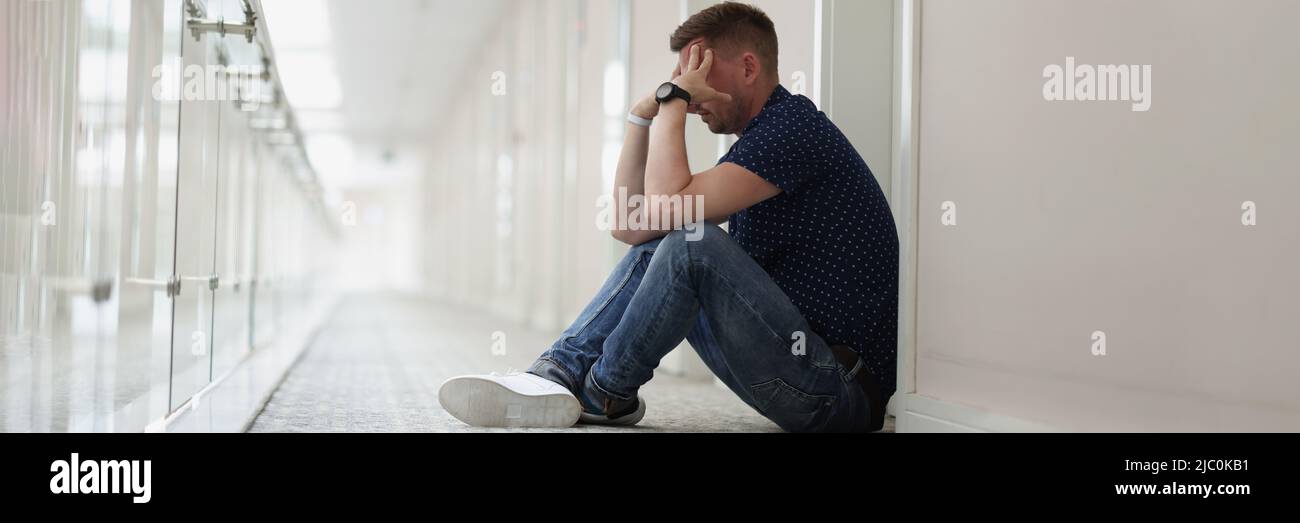 Upset man sitting on floor in hallway Stock Photo