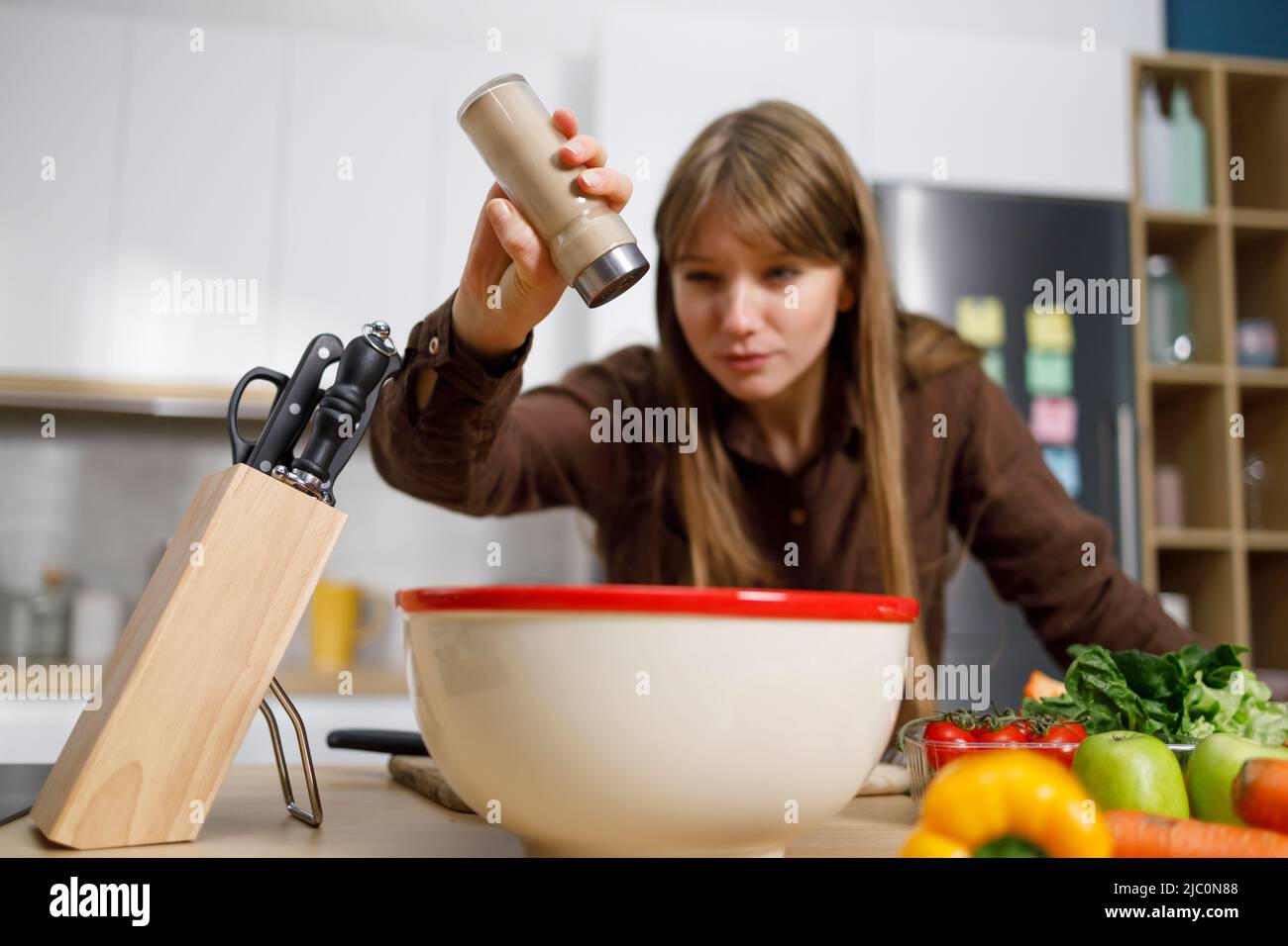 Young woman cooking in the kitchen adding pepper into the bowl Stock Photo