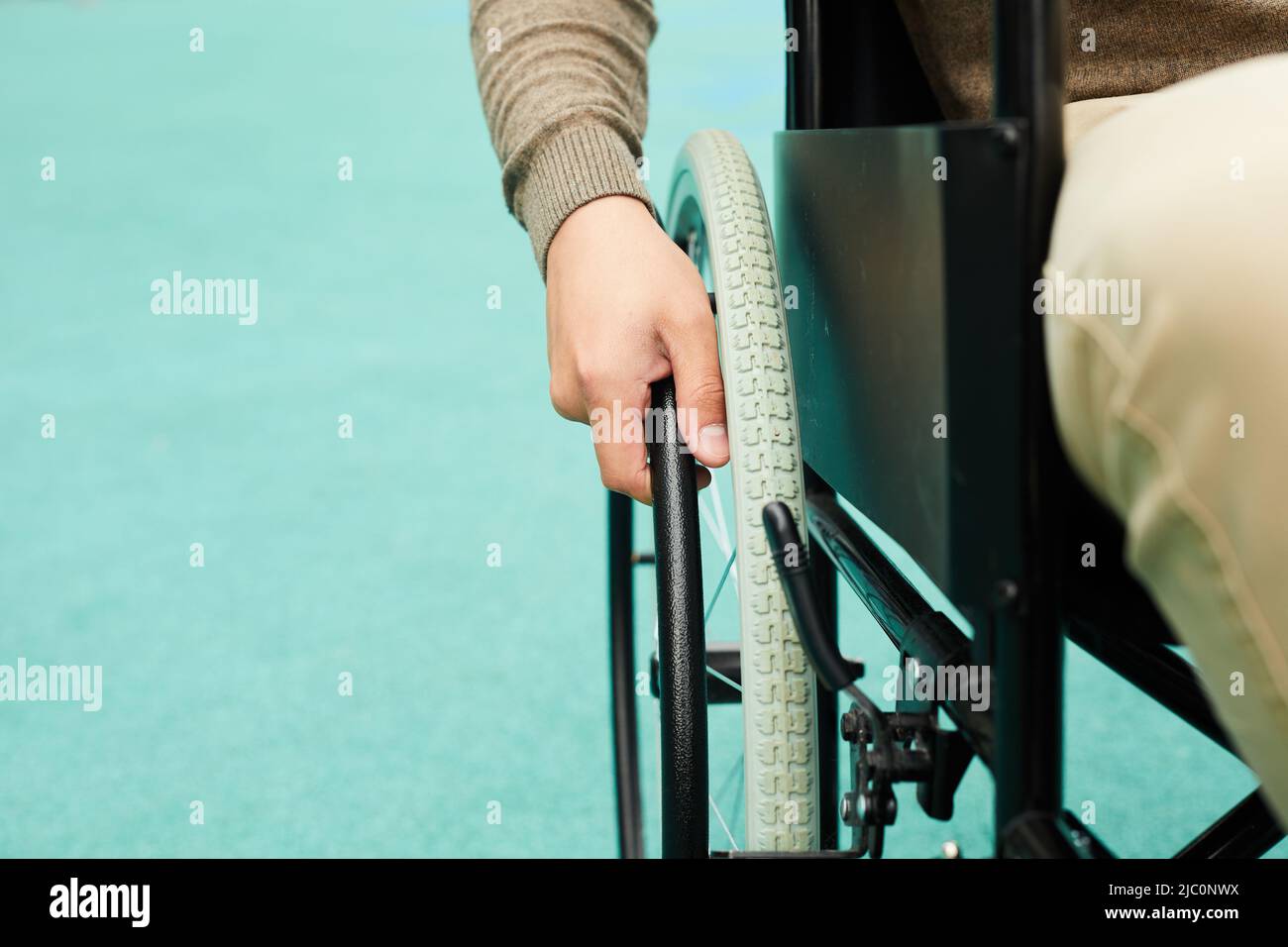 Close-up of unrecognizable handicapped man pushing hand rim of wheelchair while moving outdoors Stock Photo