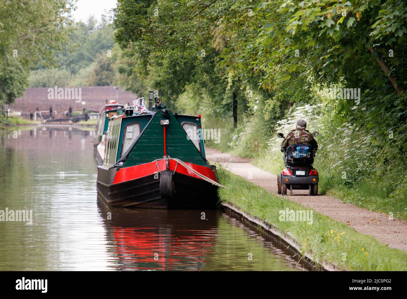 A disabled person on a mobile scooter making their way along a canal towpath unassisted. Picture shows how a good pathway alongside the canal can improve the life of a disabled person. Stock Photo