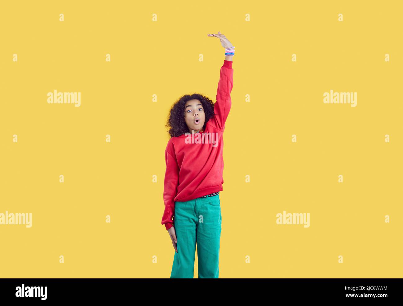 Funny pretty African American girl wants to grow taller and measures her height Stock Photo
