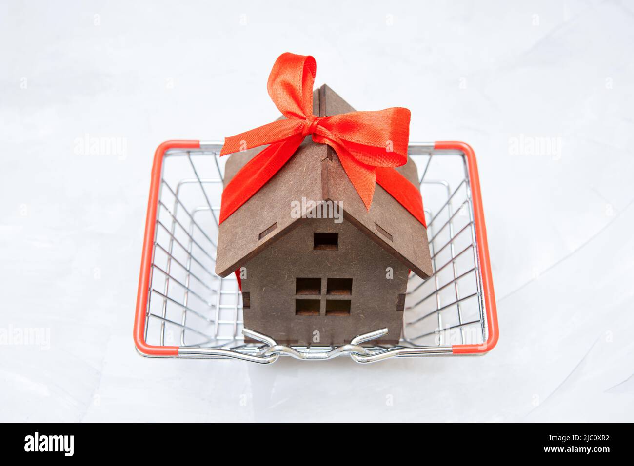 Wooden toy house decorated with a red ribbon and a bow in a tiny shopping cart. Home buying concept. Stock Photo