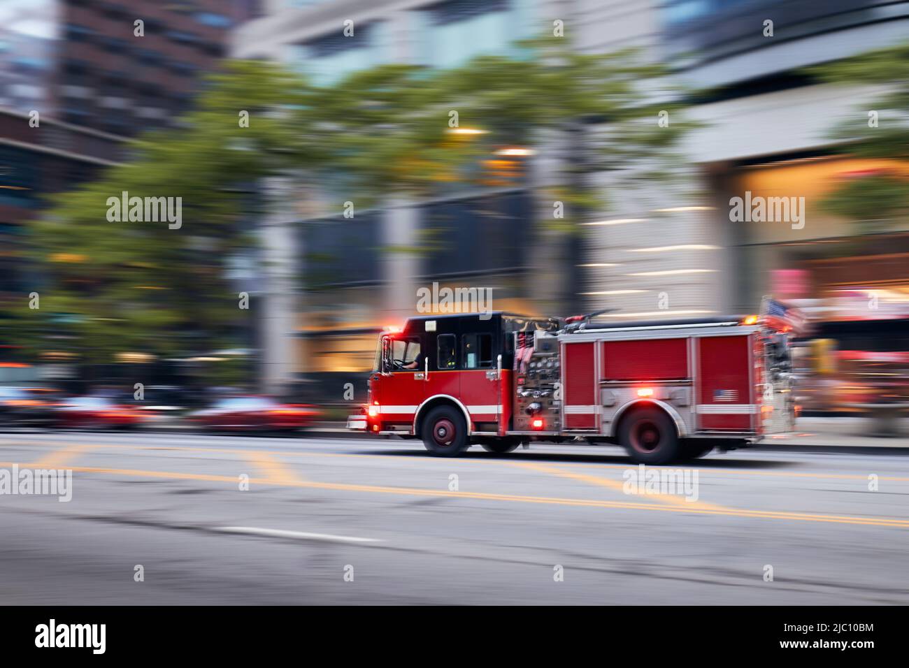 Fast moving fire engine on city street. Firefighters in blurred motion. Themes rescue, urgency and help. Stock Photo