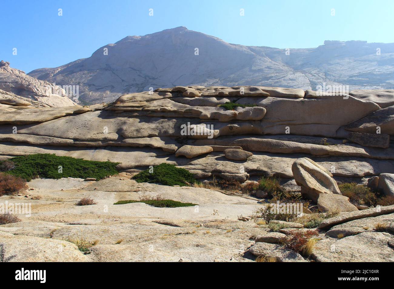 Volcanic layered flat rocks with green bushes in the Bektau-Ata tract against the backdrop of a large mountain Stock Photo