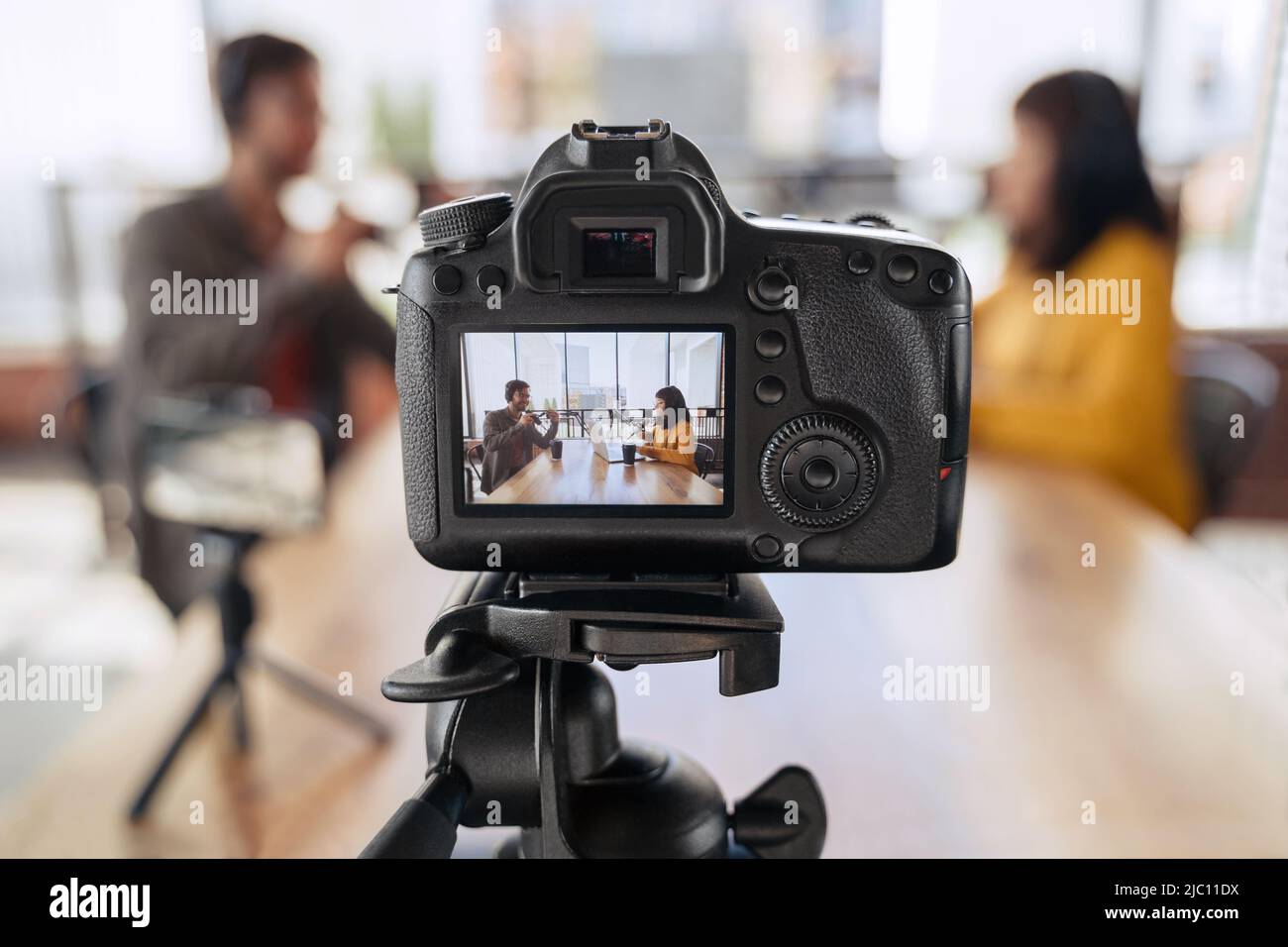 Close up of professional camera recording podcast interview of two bloggers. Man and woman podcasters in headphones talking with each other while shooting video podcast or vlog in broadcasting studio Stock Photo