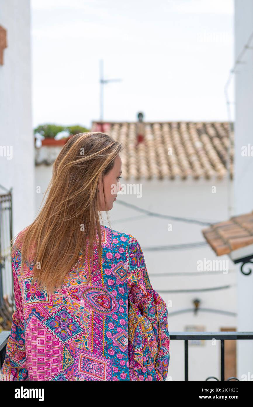 woman seen from behind on balcony overlooking rural village street Stock Photo