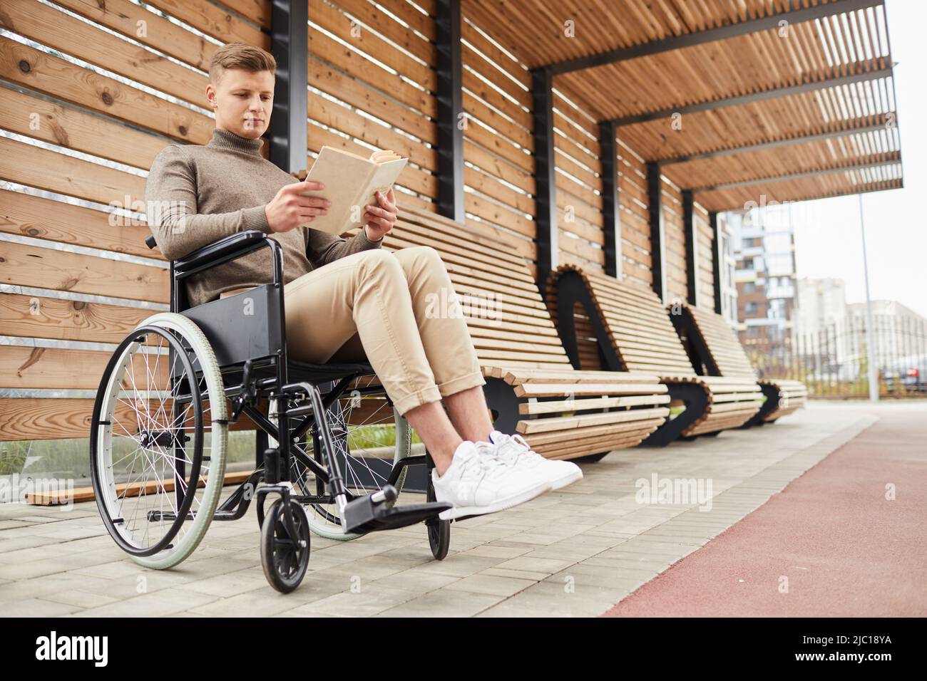 Serious handicapped young man in white shoes sitting in wheelchair at