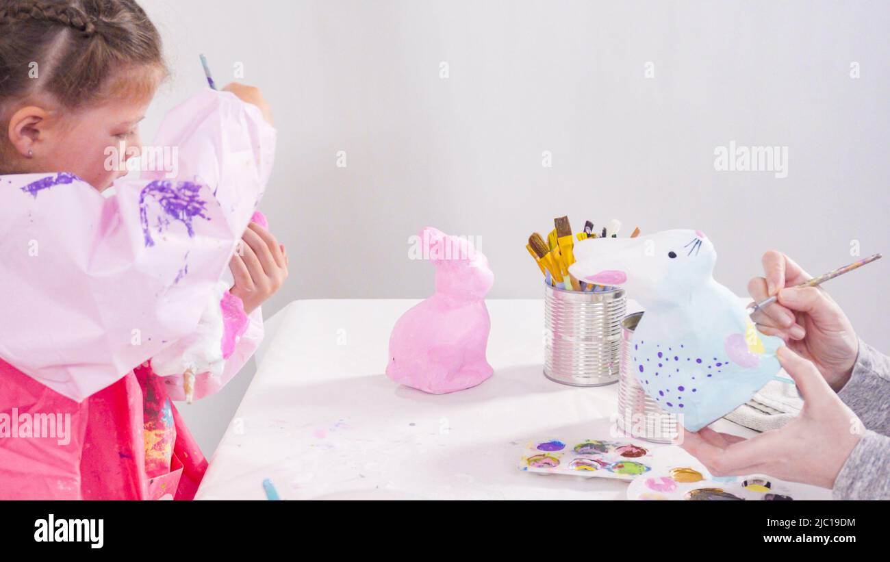 Little girl painting paper mache figurines with acrylic paint for her