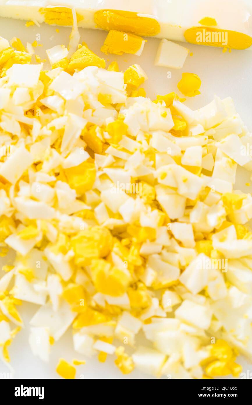 Cutting hard-boiled eggs in a shape of a loaf on a white cutting board. Stock Photo