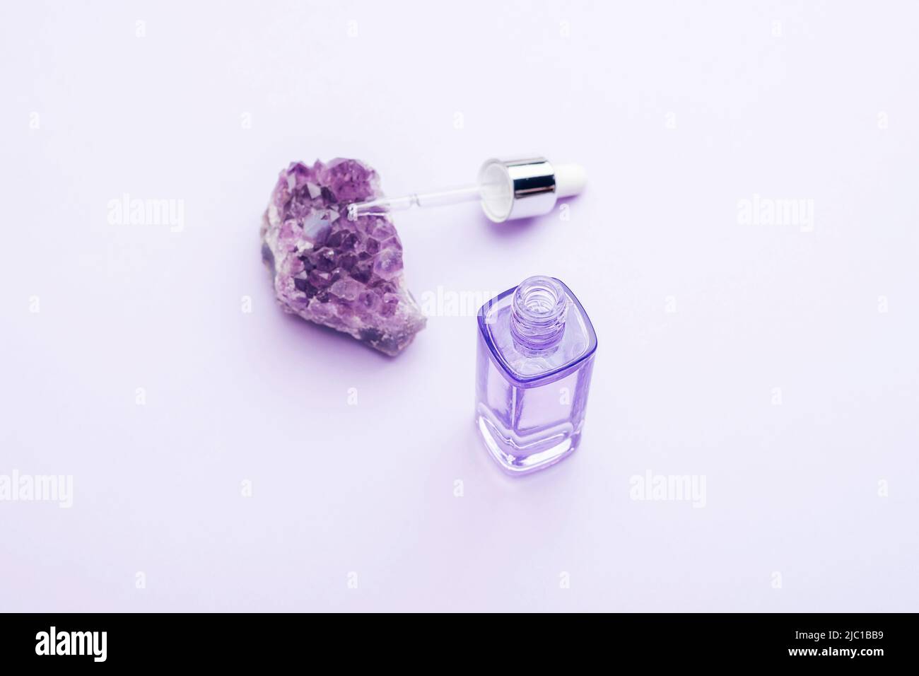 Purple serum bottle with pipette and amethyst crystal, top view. Natural cosmetics concept. Selective focus. Stock Photo