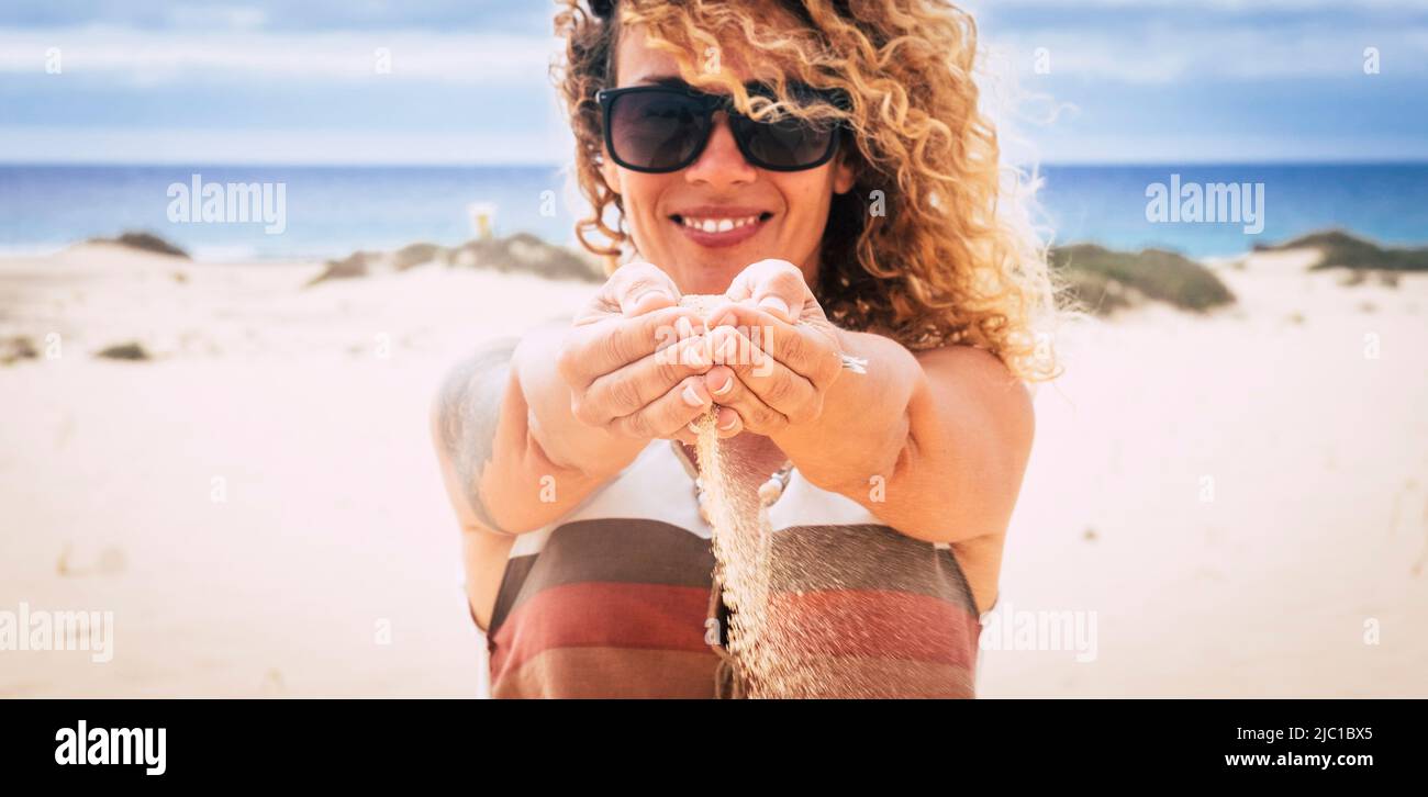 Cheerful woman in summer holiday vacation enjoy the beach and the sun falling sand from her hands and smiling at the camera. Happy tourist with ocean Stock Photo