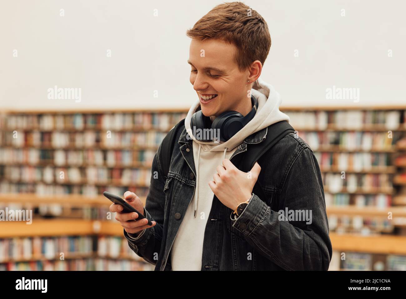Smiling student using smartphone while standing in library Stock Photo