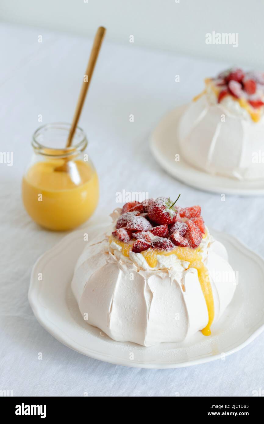 Classic Pavlova desserts with strawberry, whipped cream and lemon curd and jar with lemon curd. Stock Photo