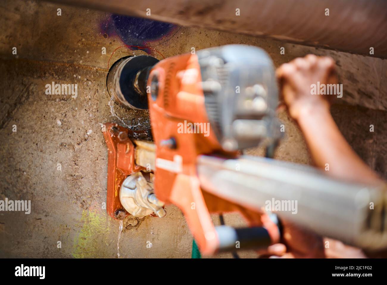 A construction working uses an industrial water-fed core drill to cut through an exterior concrete retaining wall. Stock Photo