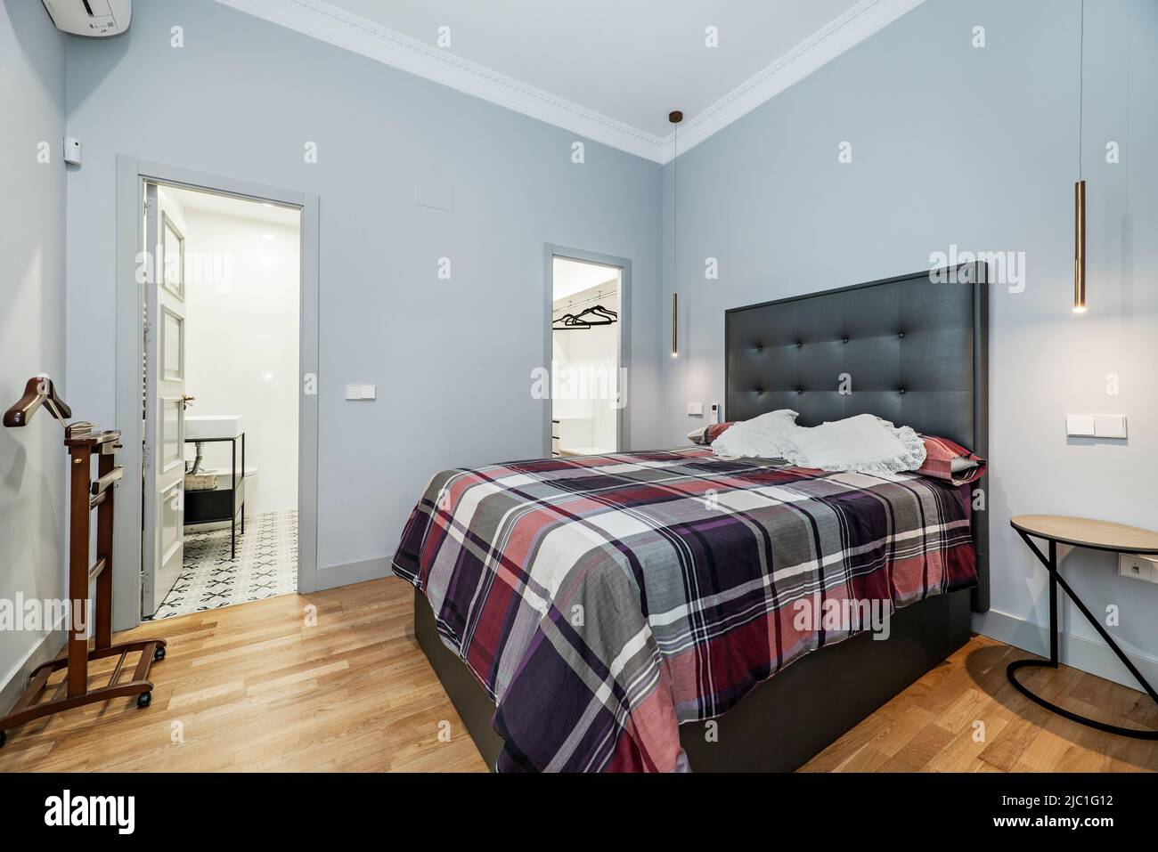 Bedroom with designer double bed, gray dressing room door and en-suite bathroom, night coat and oak wood flooring Stock Photo